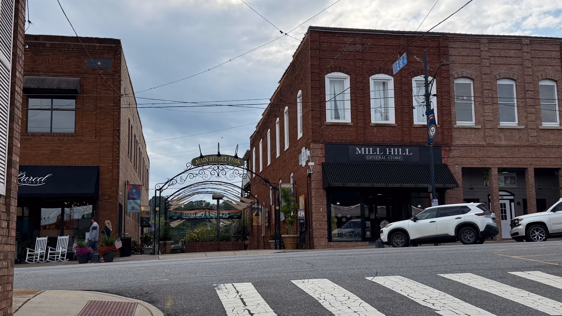 Brick storefronts line a small-town street with a crosswalk and parked cars.