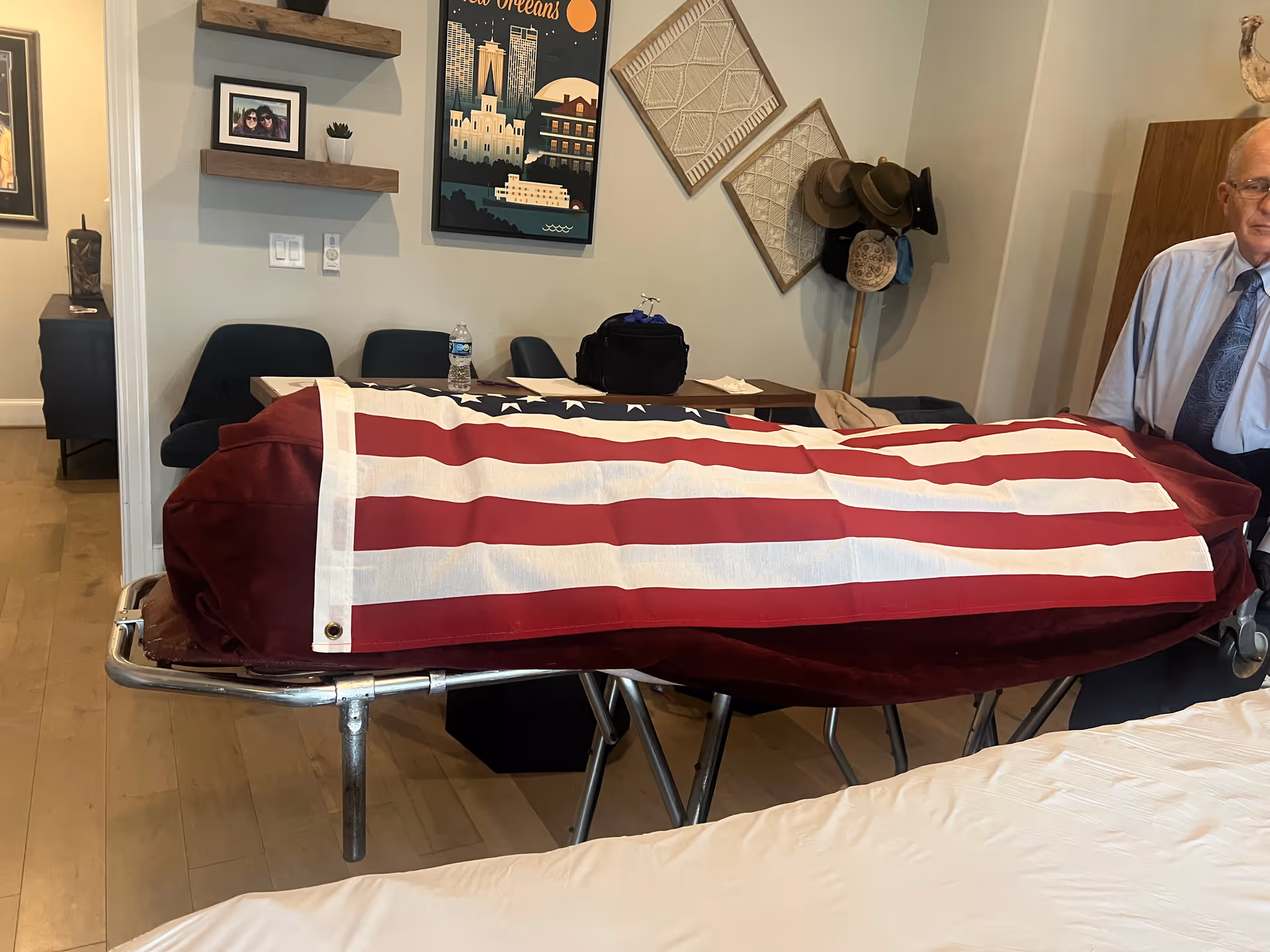 Flag-draped coffin on a wheeled gurney inside a hospice facility room.