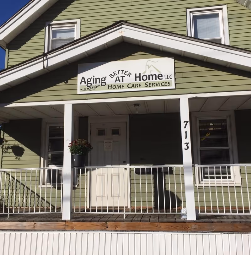 Green building exterior with white porch and a sign reading Aging Better At Home LLC.