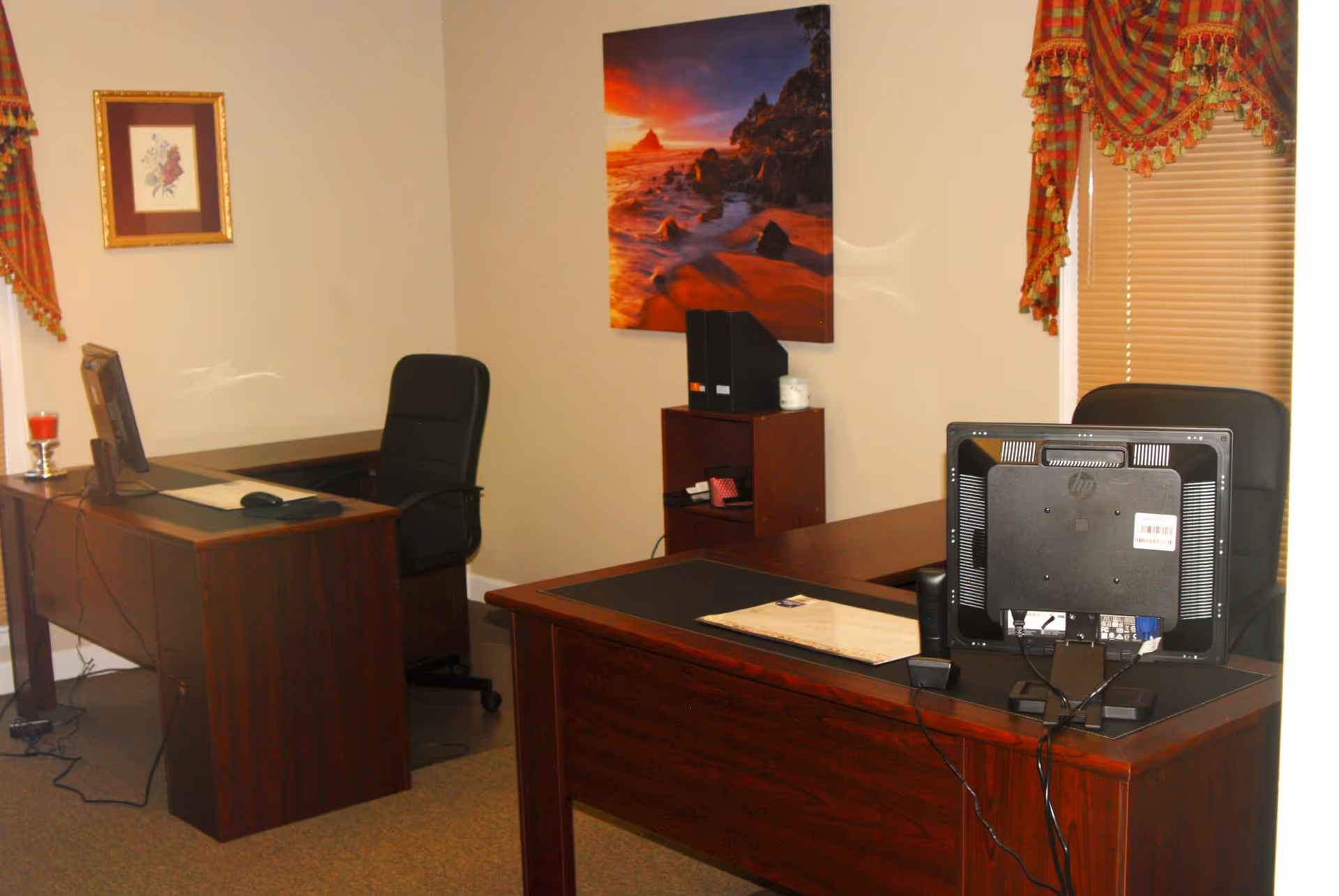 Two desks with computers in a small, furnished office with wall art.
