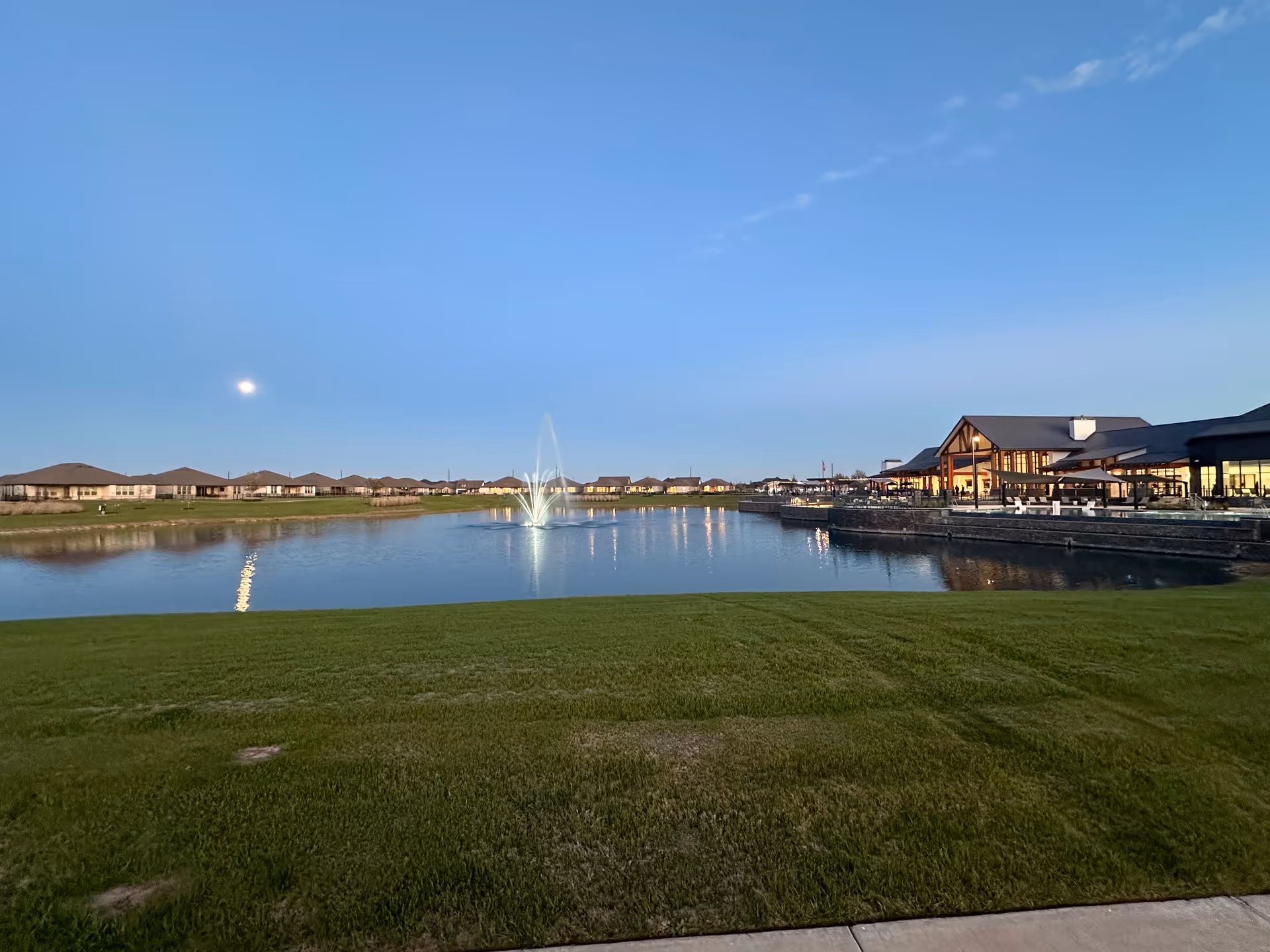 Wide outdoor lawn overlooking a pond with fountain and campus buildings.