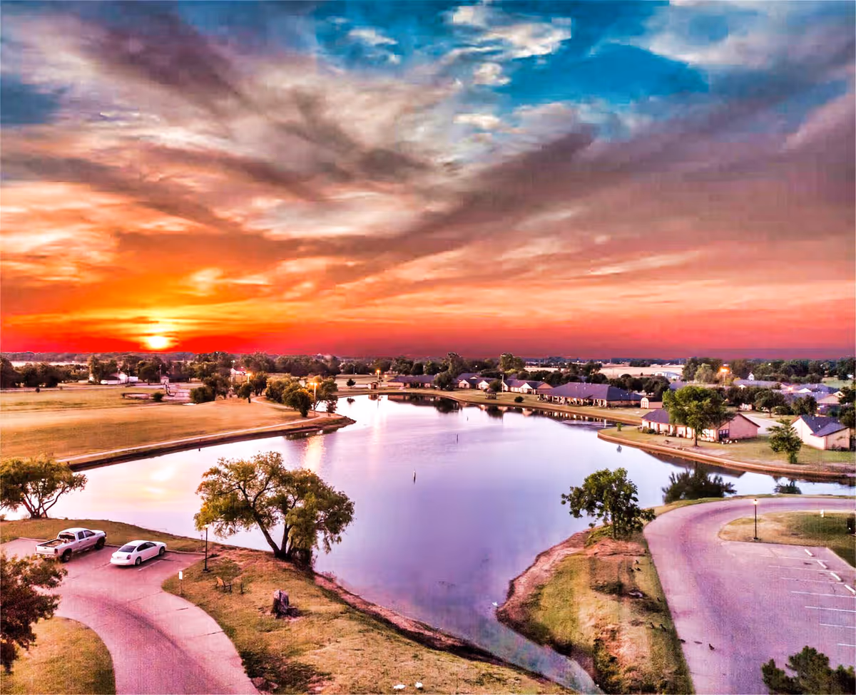 Aerial sunset view of a lakeside residential community with roads and trees.