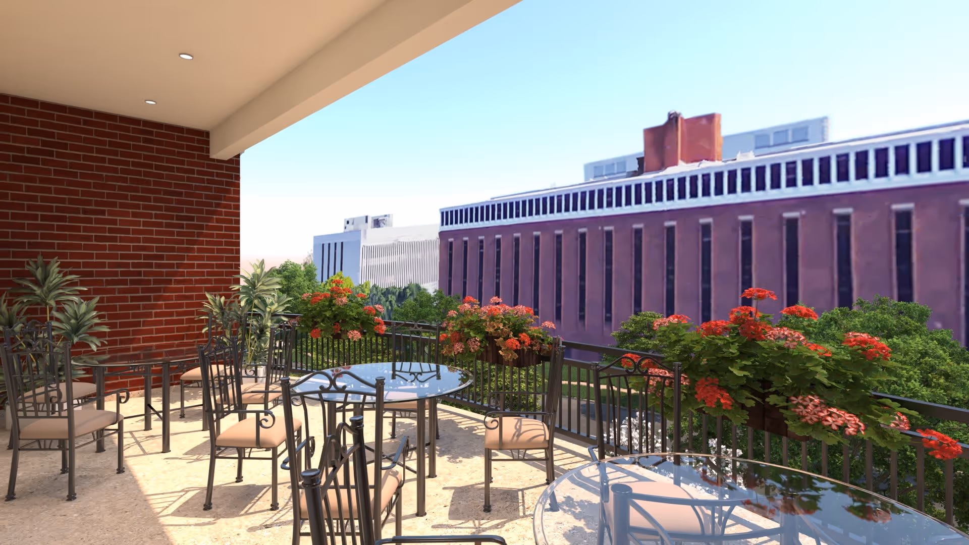 Outdoor balcony area with several glass-top tables and metal chairs with cushions, surrounded by flower boxes filled with red and pink flowers. The balcony overlooks a cityscape with large buildings and greenery under a clear blue sky.