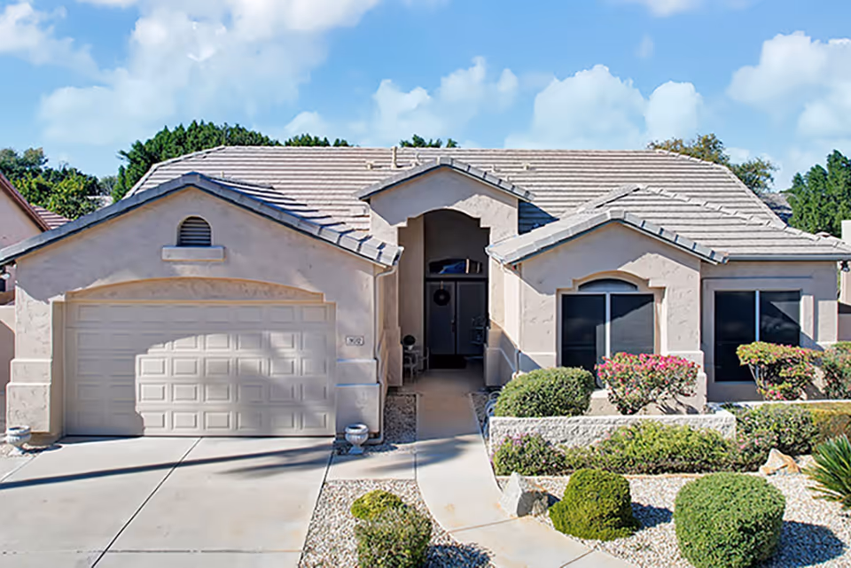 A single-story beige assisted living home with a two-car garage and landscaped front yard.