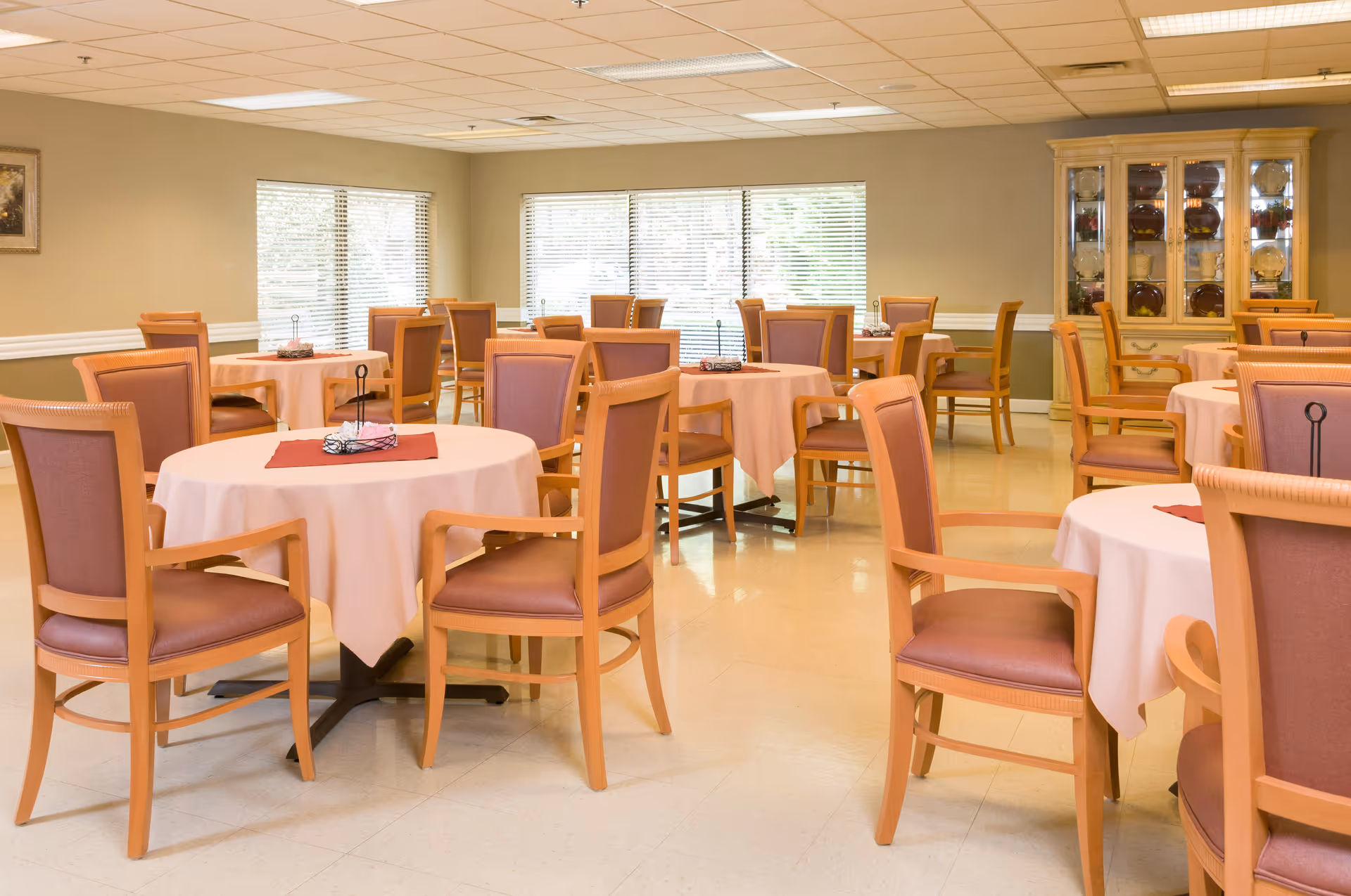 Light-filled dining room with round tables, pink tablecloths, and wooden chairs.