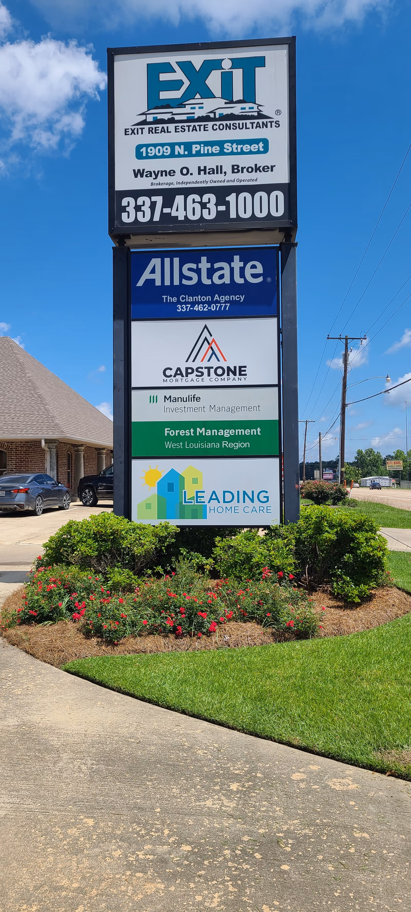 Tall outdoor signpost displays multiple business signs, including Leading Home Care, in a landscaped lot.