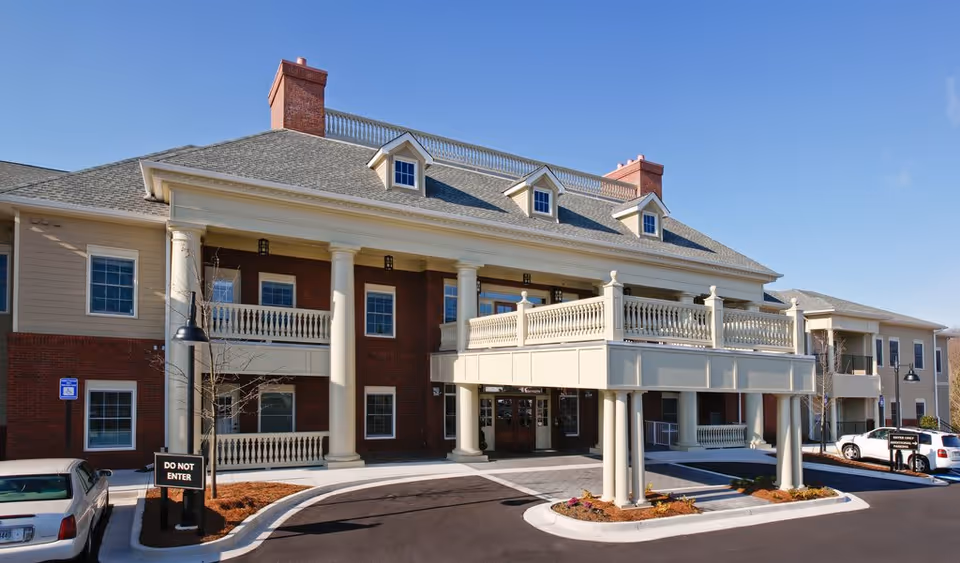 Front exterior of Gardens of Gainesville showing the main entrance with large columns, a covered porte-cochère, balcony railings and parked cars.