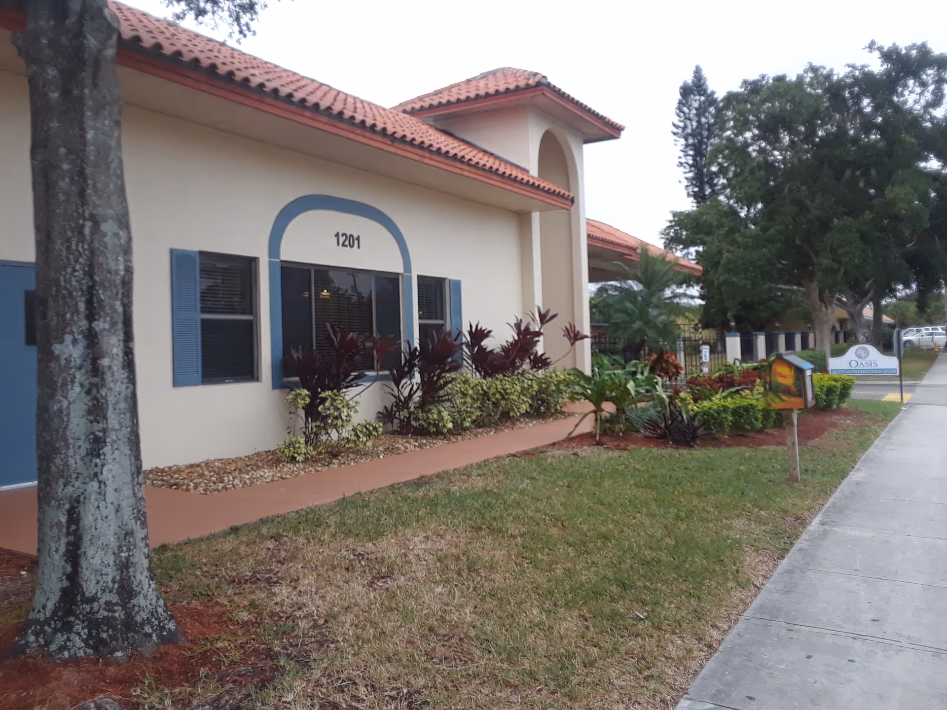 Front exterior of Lake Worth Rehabilitation Center with beige walls, blue shutters, and a walkway.