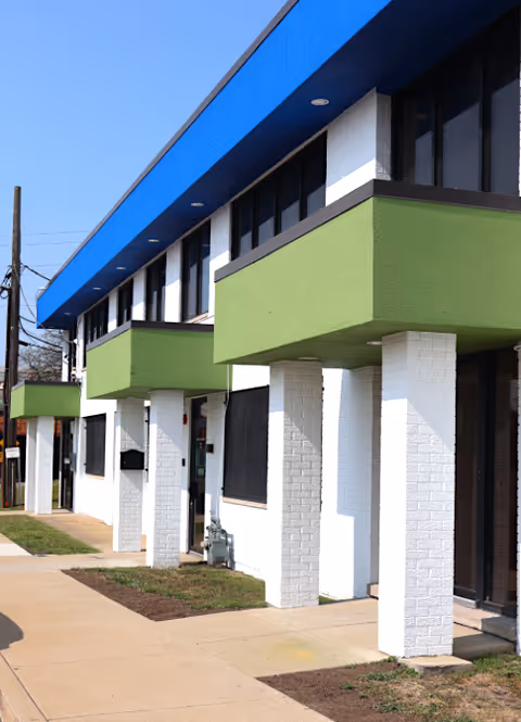 Exterior of a two-story building with white brick columns and green awnings along a sidewalk.