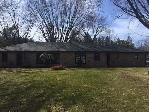 Single-story brick building with a grassy front yard and leafless trees in background.