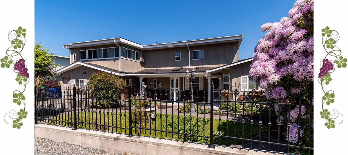 Exterior view of a senior living facility with a black fence and flowering shrubs.