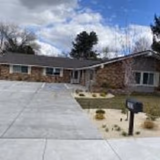 Front exterior of a single-story brick senior living facility with a long driveway and mailbox.