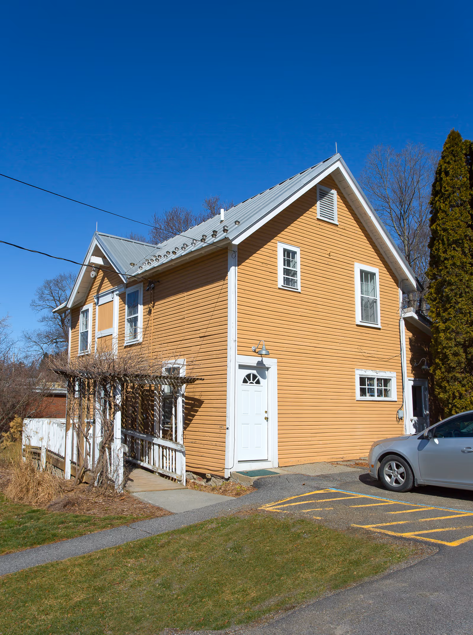 Orange wooden building with white trim under a clear blue sky and parked car.