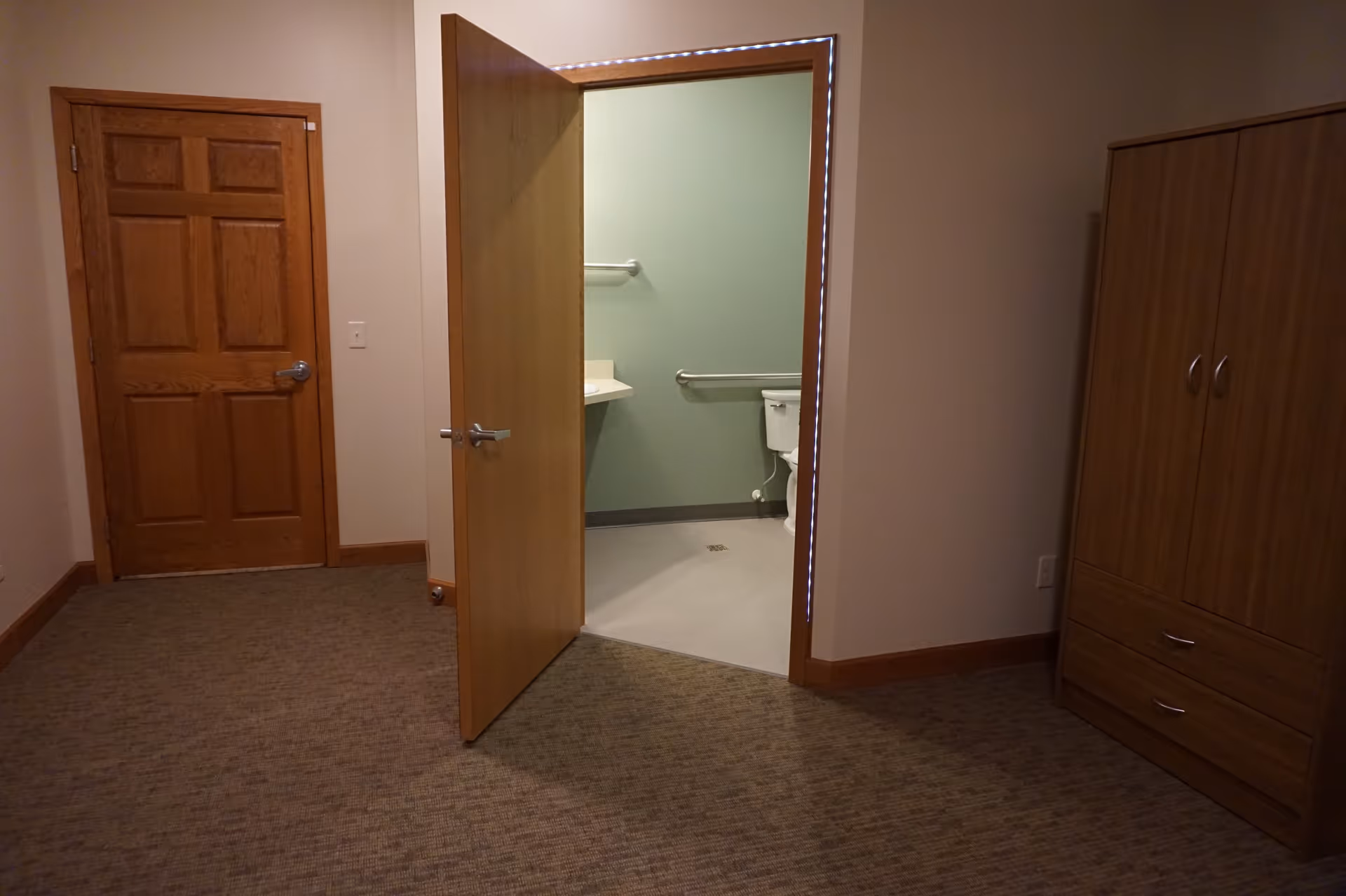 Empty corridor in Birchwood Cottage II with an open bathroom doorway and accessible grab bars.