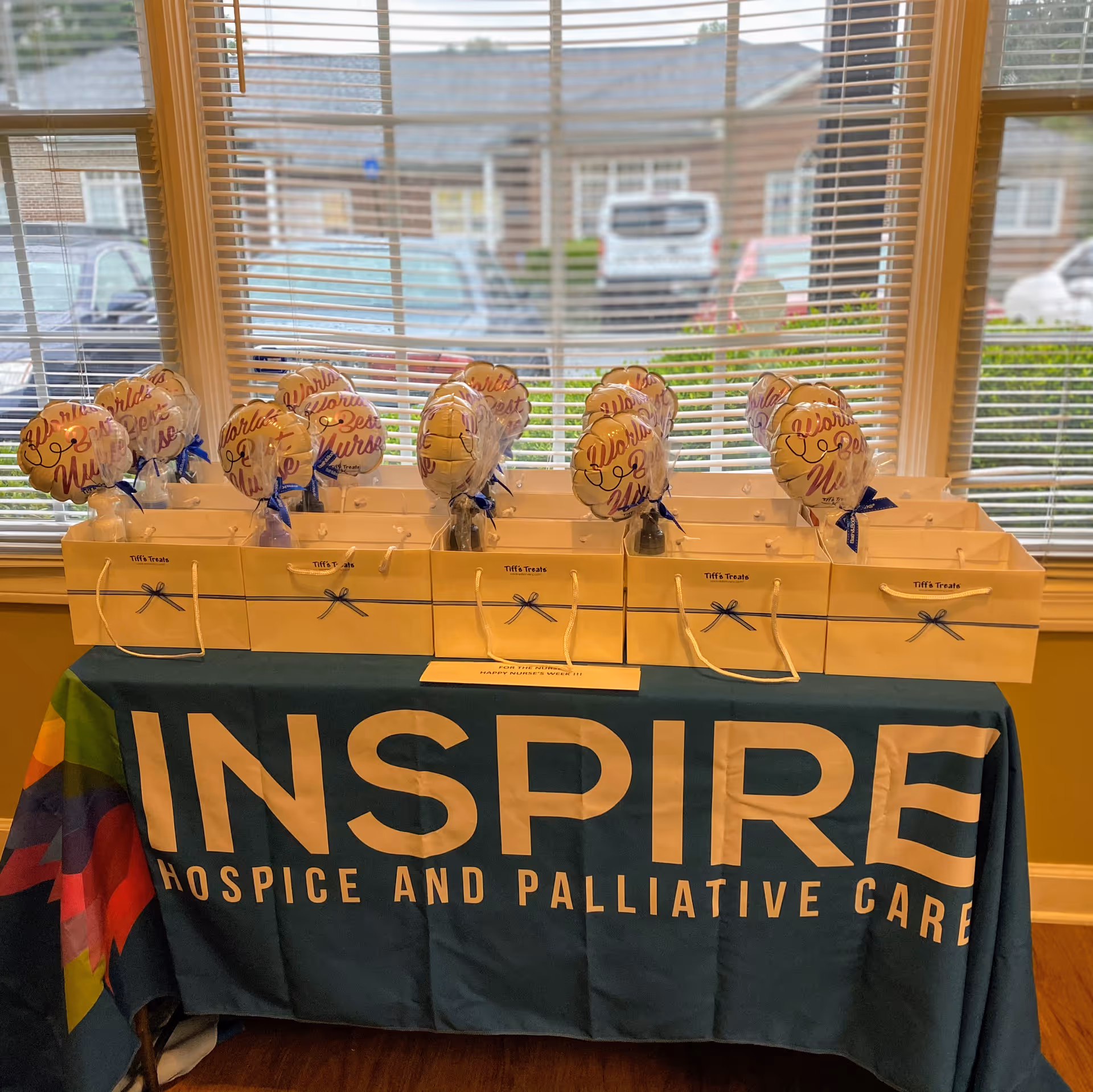 Table with gift bags and heart balloons, banner shows Inspire Hospice and Palliative Care.