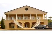Two-story beige building with curved staircases and parked cars outside.