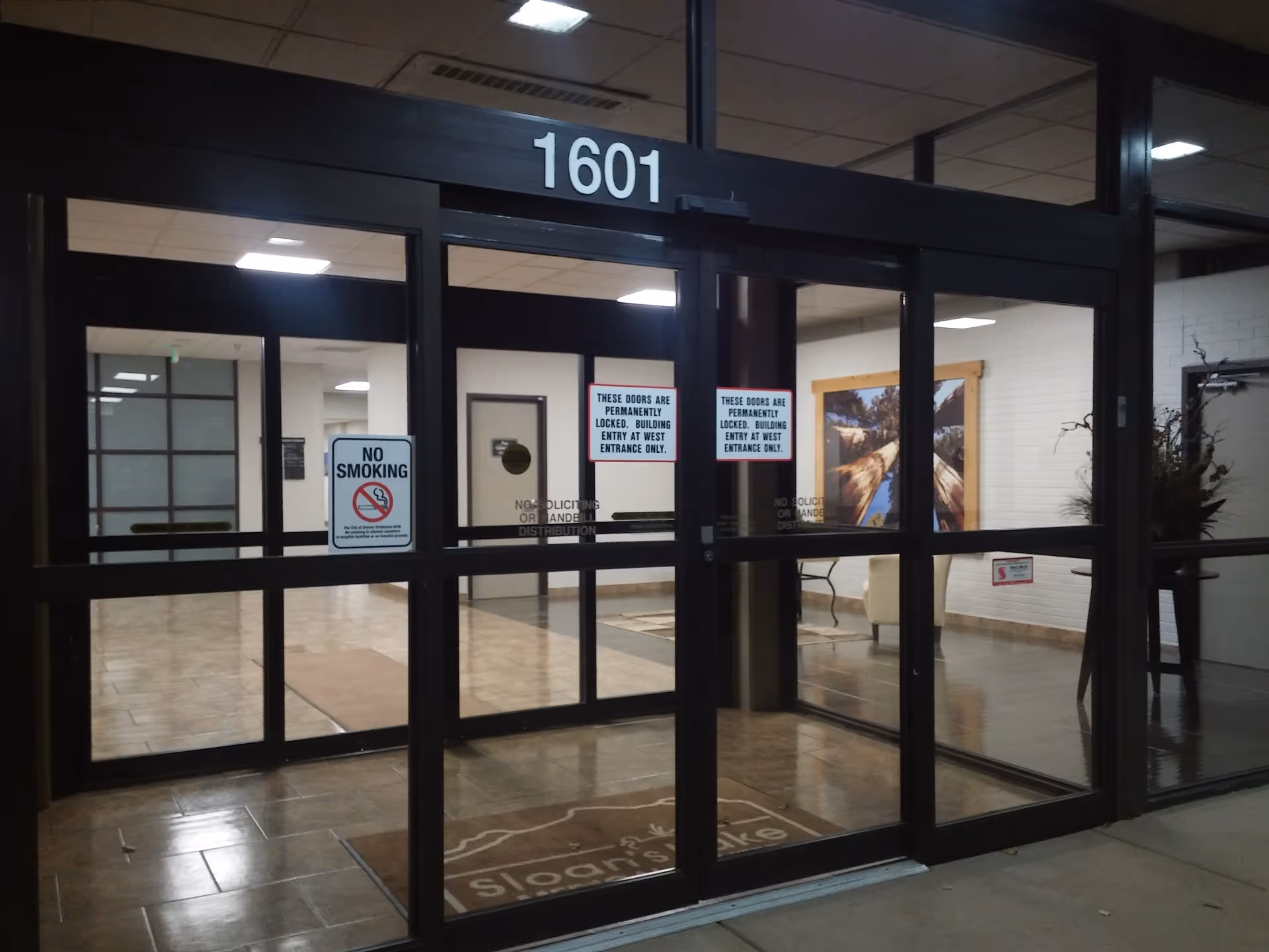 Glass storefront entrance with black frames, numbered 1601, and posted signs in lobby.