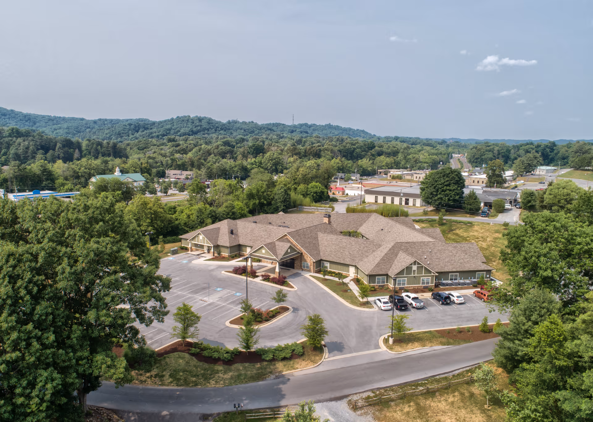 A large, single-story senior living facility with parking, surrounded by trees and hills.