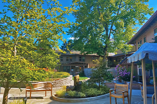 Sunny courtyard at Marie Rose Center Assisted Living with trees, benches, and an awning.