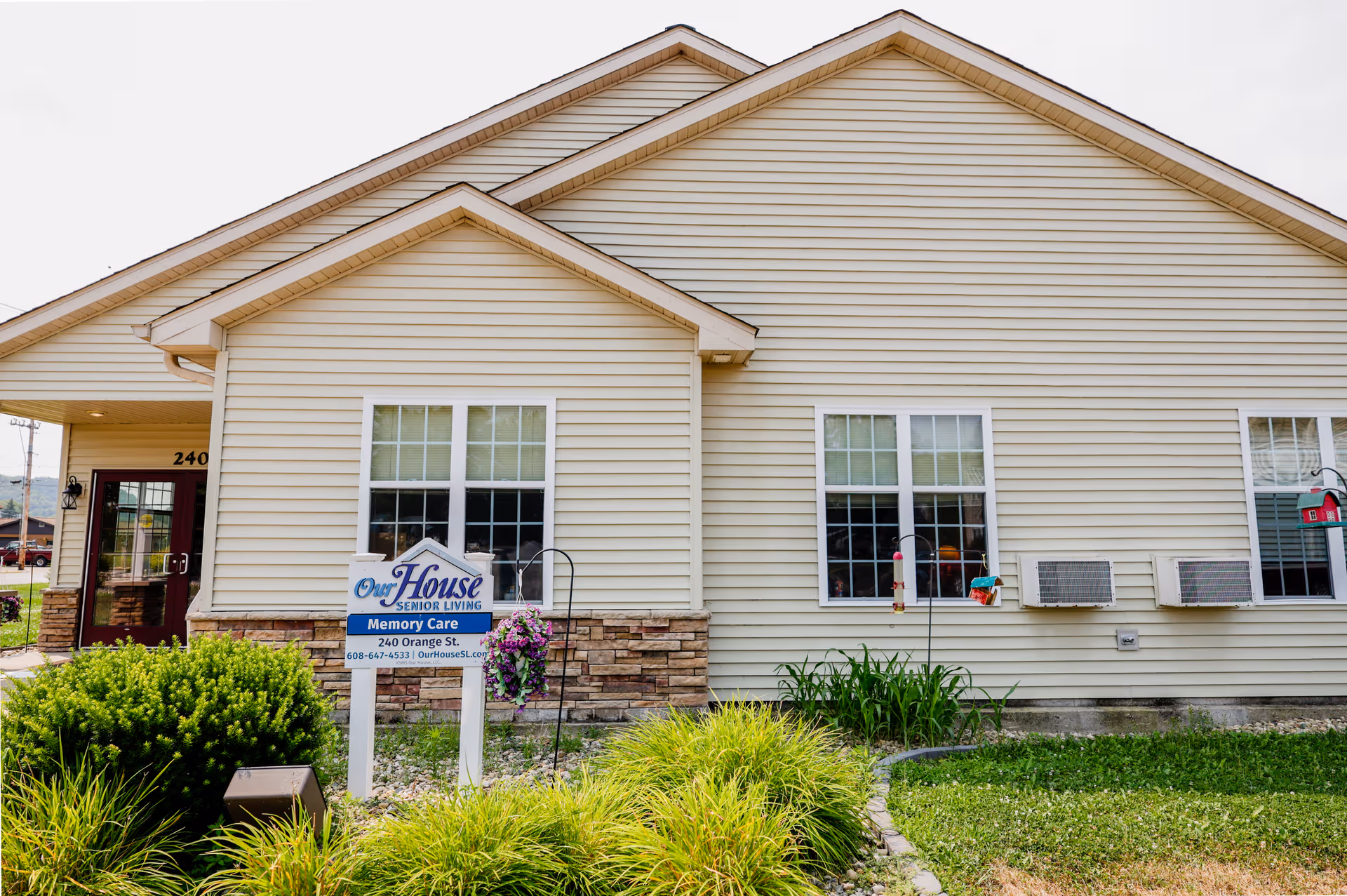 Beige senior living facility exterior with a sign and landscaped front yard
