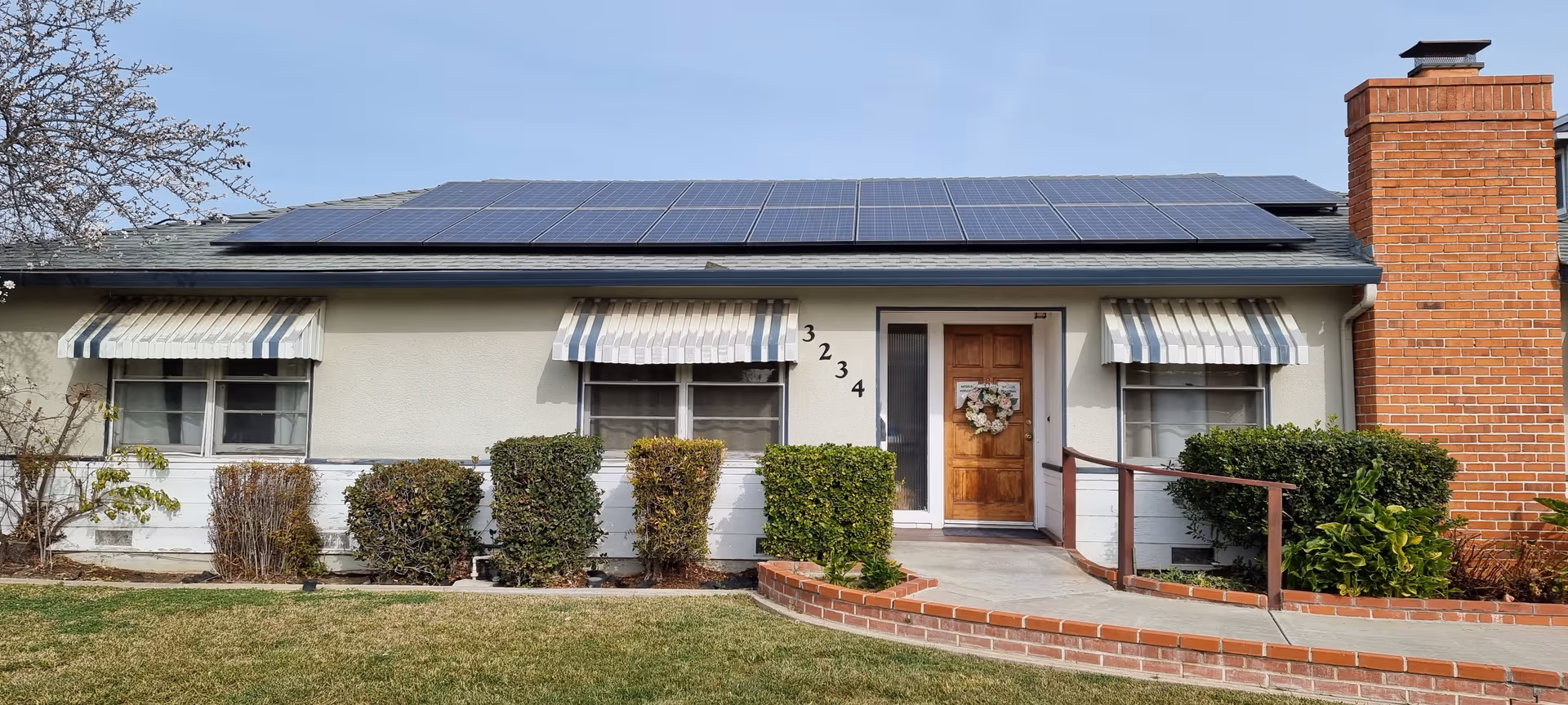 Single-story senior living facility exterior with front door, solar panels, awnings, and shrubs.
