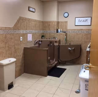 Interior bathroom at Clement Manor retirement community with accessible stalls and beige tiled walls.