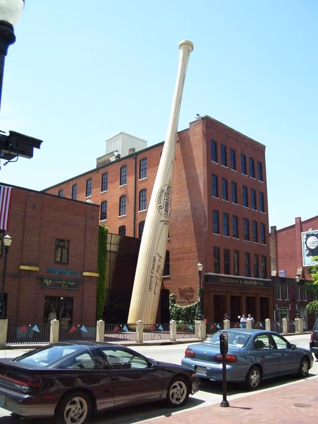 Brick building facade with a giant leaning baseball bat sculpture beside the street.