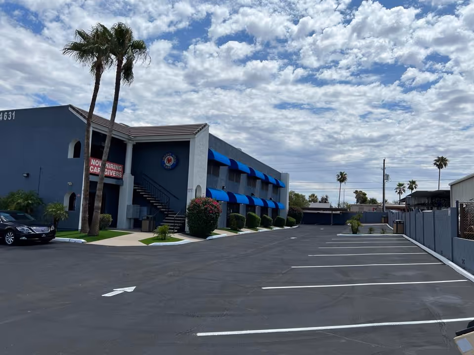 Blue-walled senior care building with blue awnings, palm trees, and a spacious parking lot.