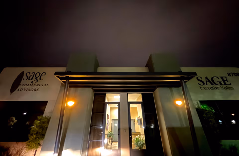 Night exterior of a building entrance with illuminated doorway and Sage signage.