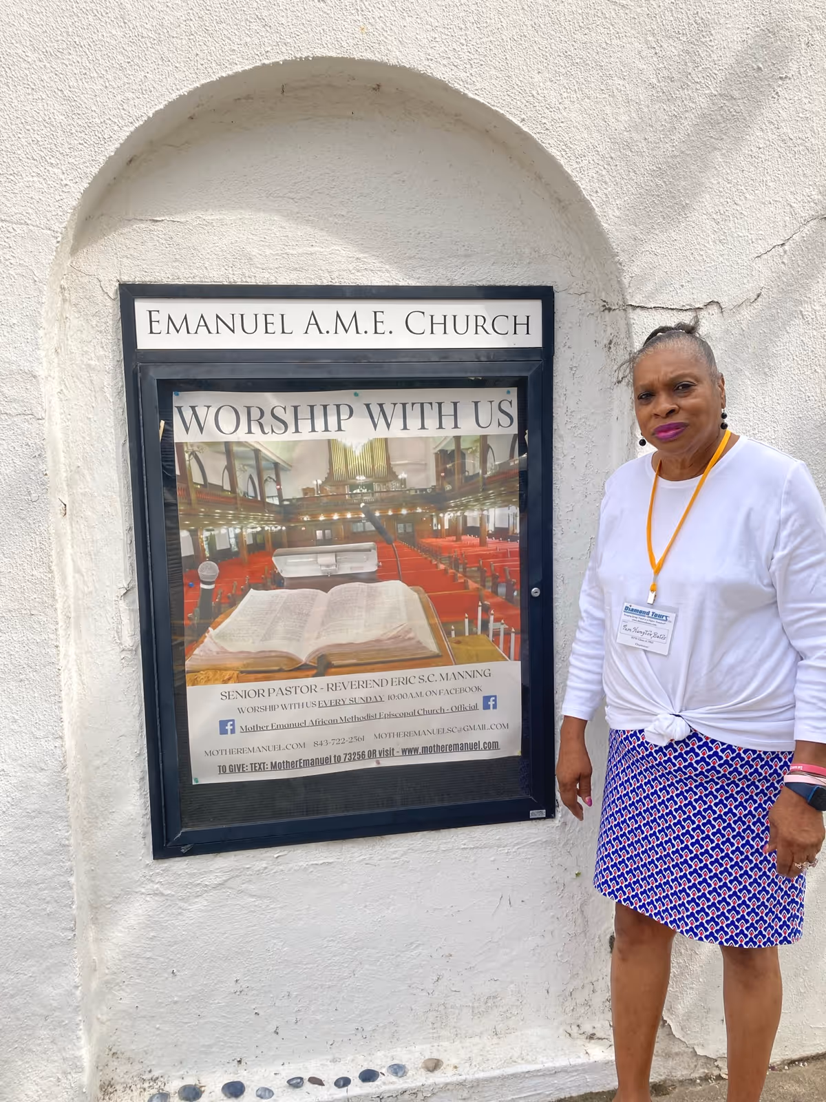 A woman stands beside a church poster mounted on a white exterior wall.