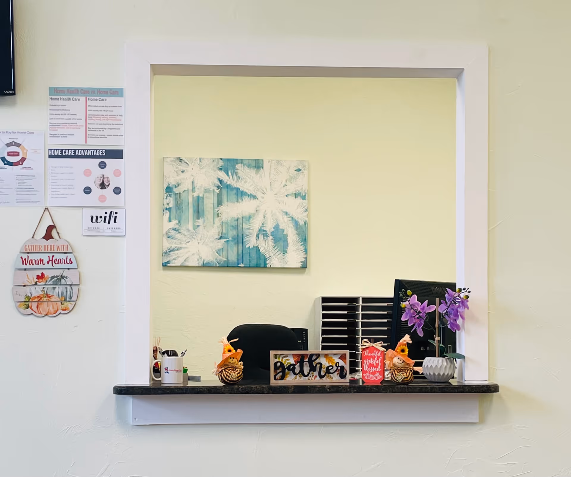 Reception desk with computer, decorations, and wall posters in a senior living lobby.