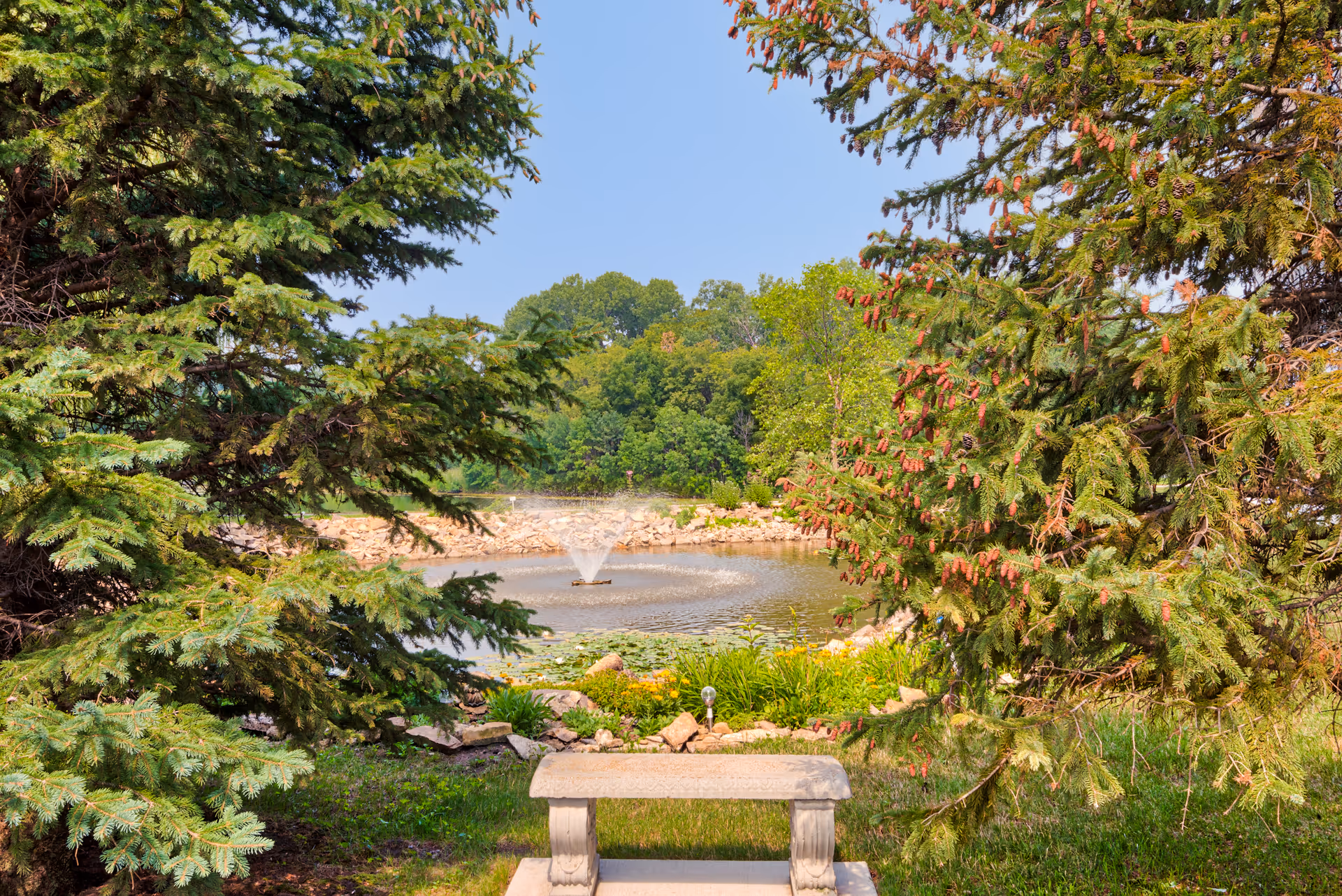 A tranquil outdoor garden with a bench overlooking a pond and fountain.