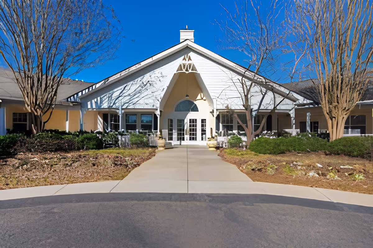 Front entrance of a single-story building with a peaked white gable, double glass doors, and a landscaped walkway.