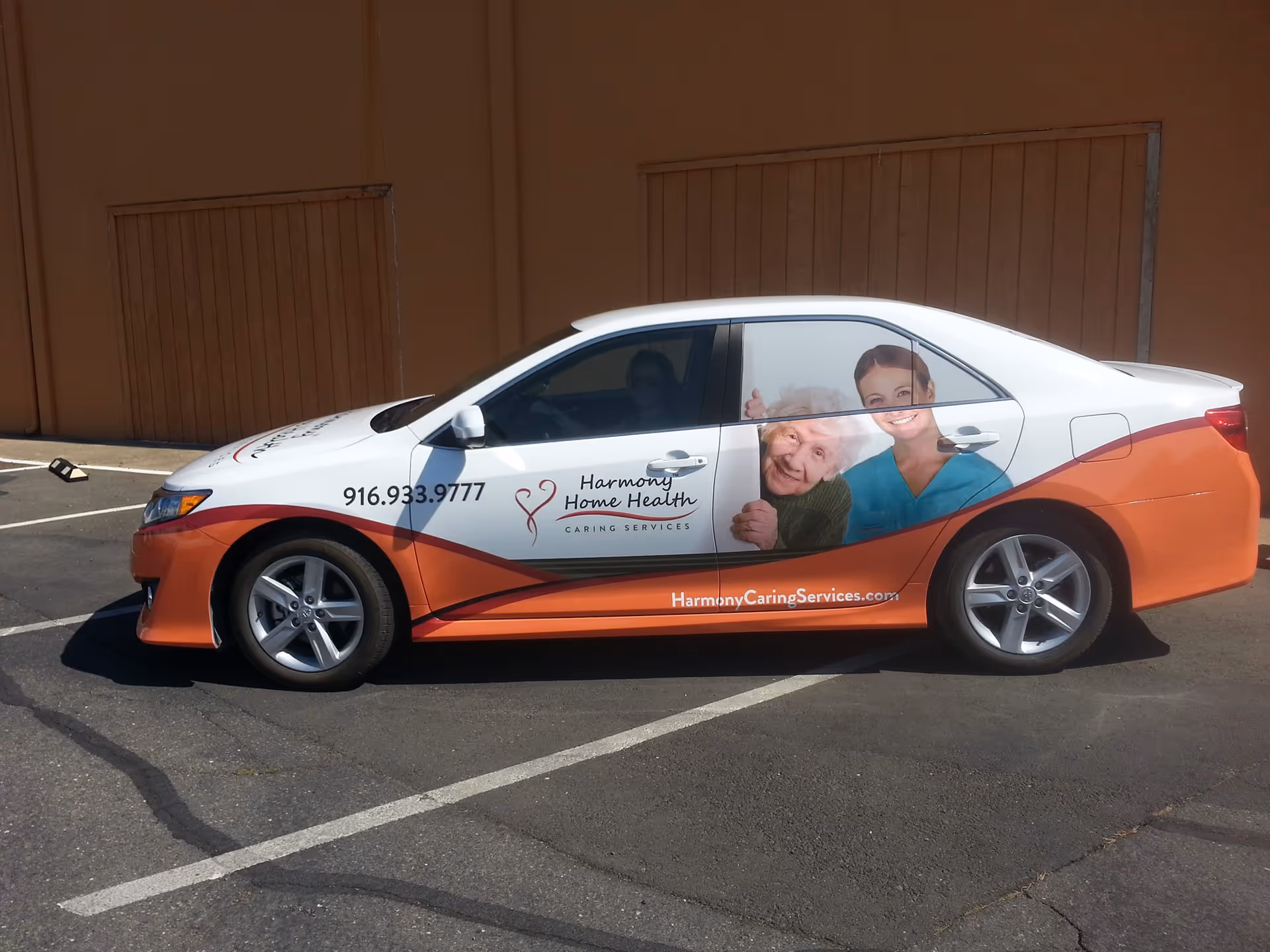 White and orange promotional car with Harmony Home Health graphics in a parking lot.