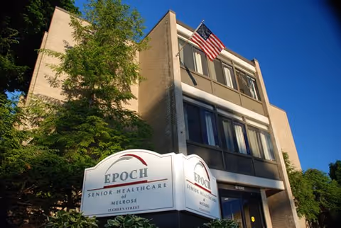 Exterior view of a multi-story senior healthcare building with sign and flag.
