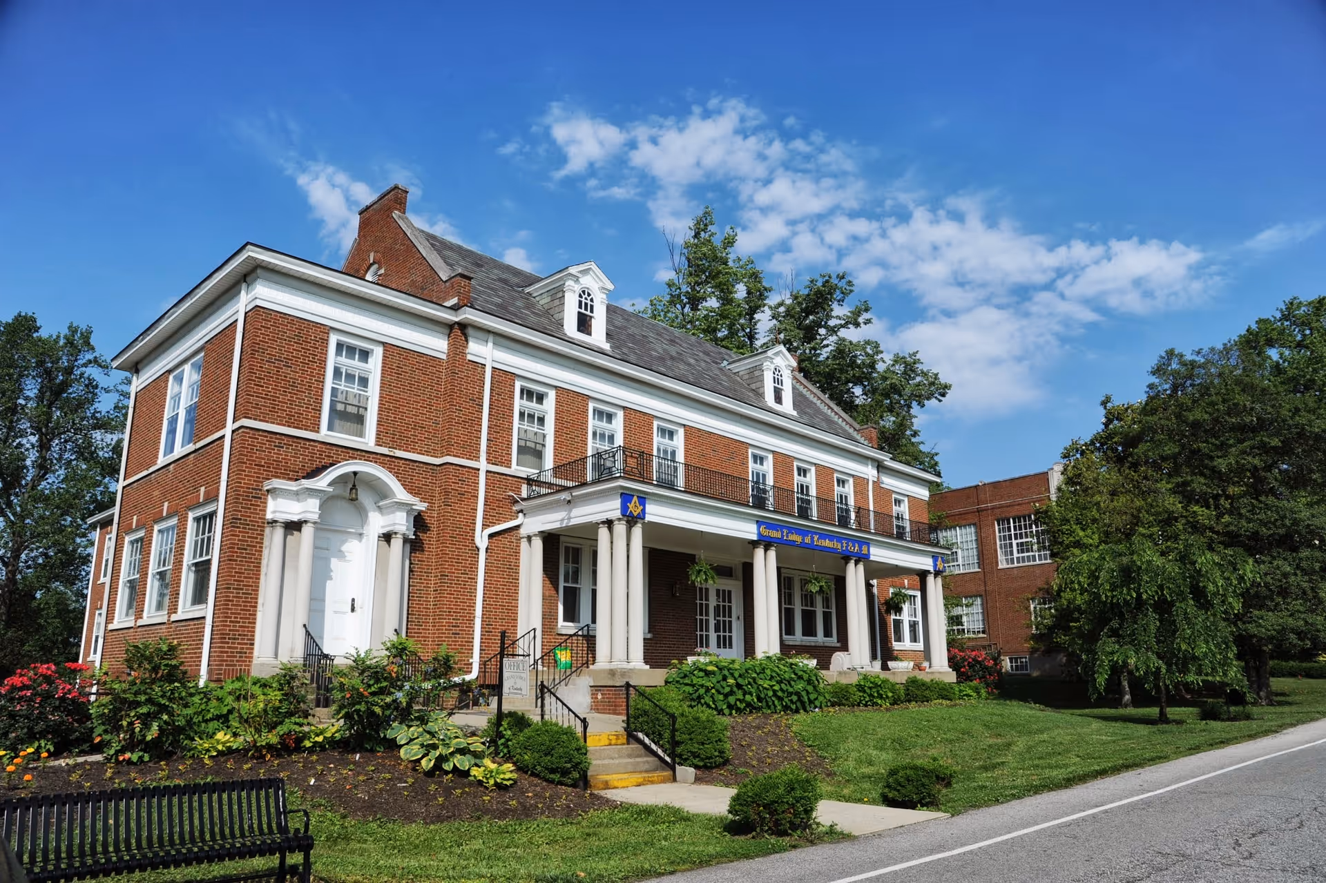 Brick senior living facility with white columns, manicured lawn, and blue sky.