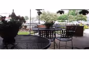Outdoor patio with metal chairs and tables, potted plants, and railing over a lawn.