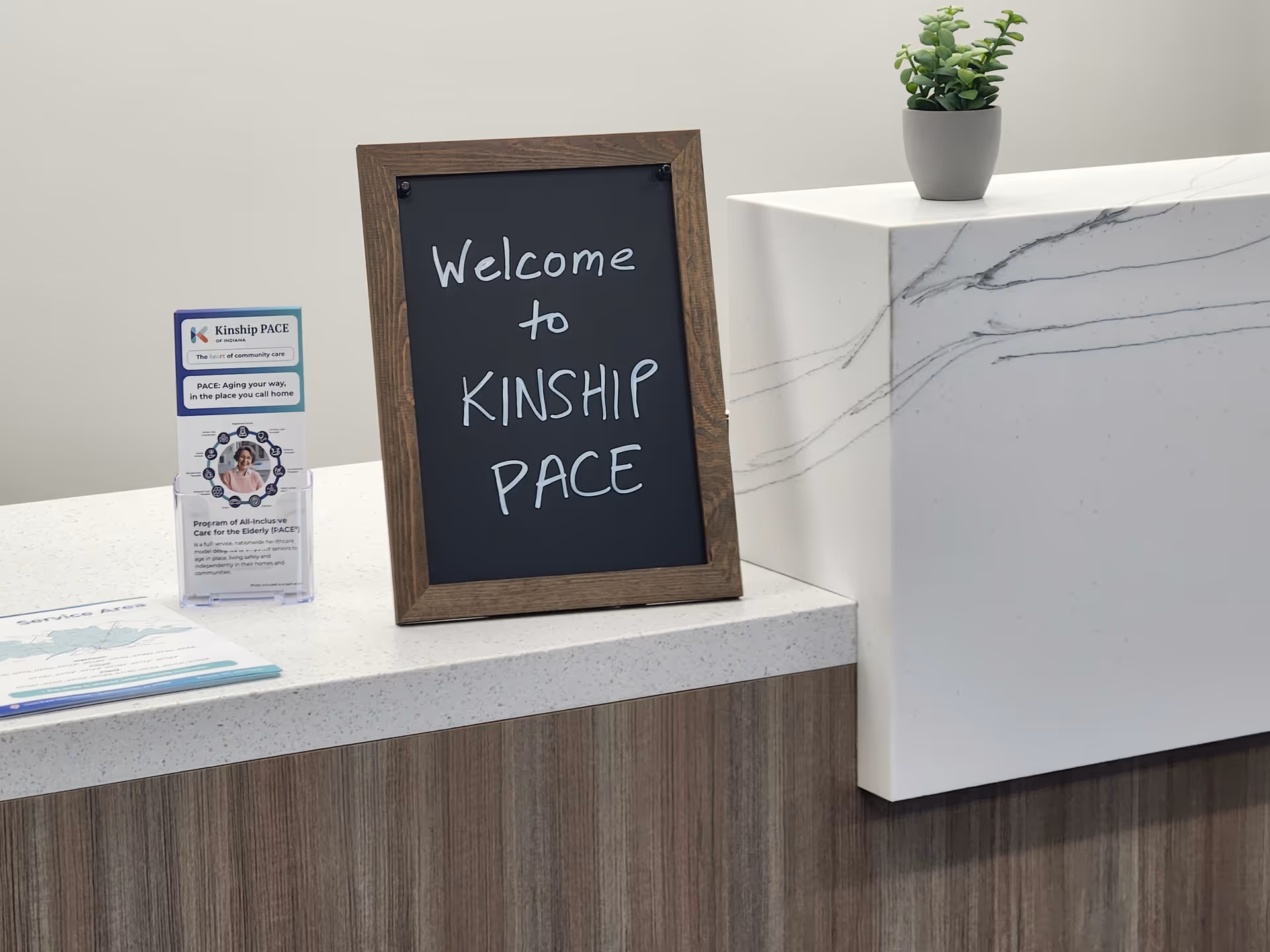 Reception area with a chalkboard sign reading Welcome to Kinship PACE on a marble counter.