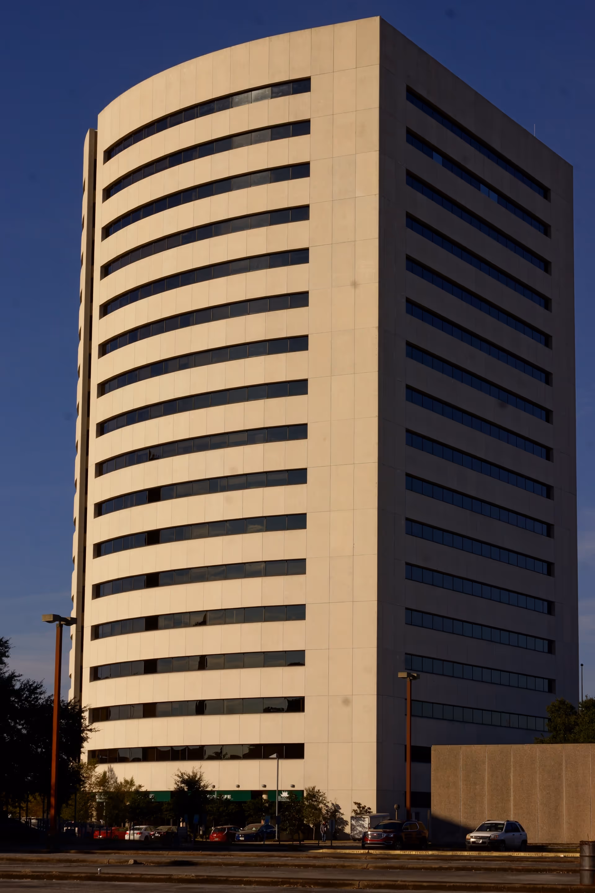 Tall curved beige building with many horizontal windows against a clear blue sky.