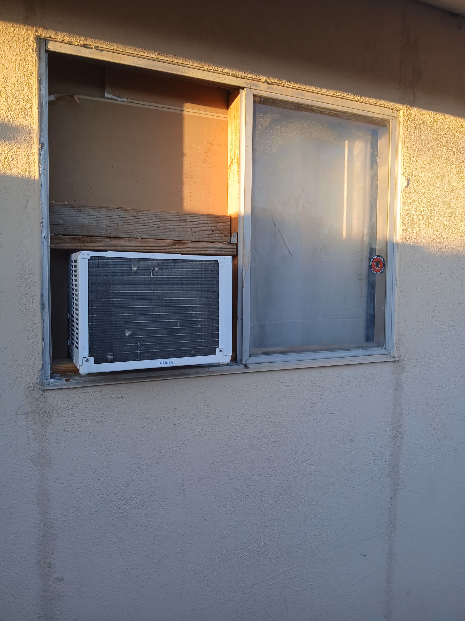 Exterior wall with a window, air conditioner unit, and worn frame.