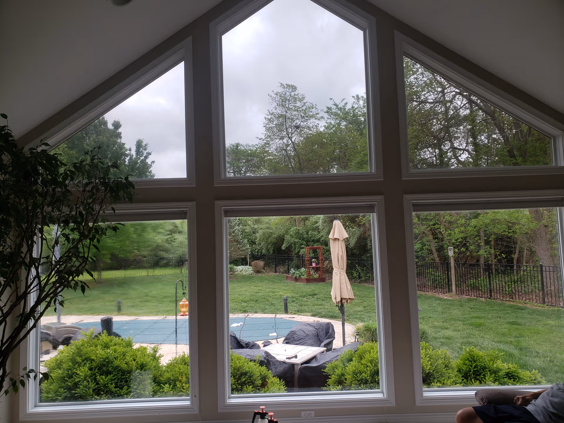 Interior room with large angled windows overlooking a green yard, pool, and umbrella.