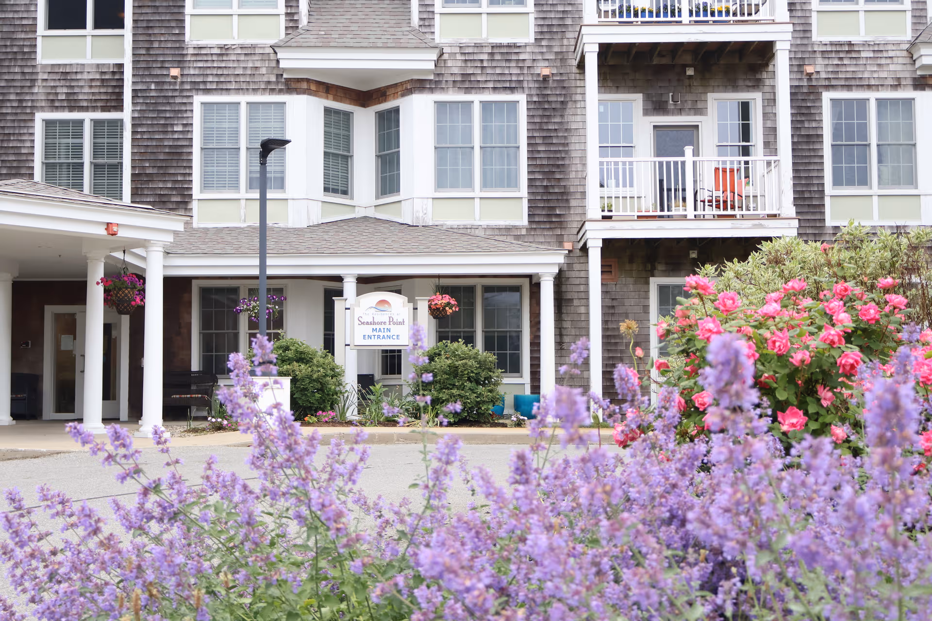 Exterior view of a senior living facility entrance with blooming foreground flowers.