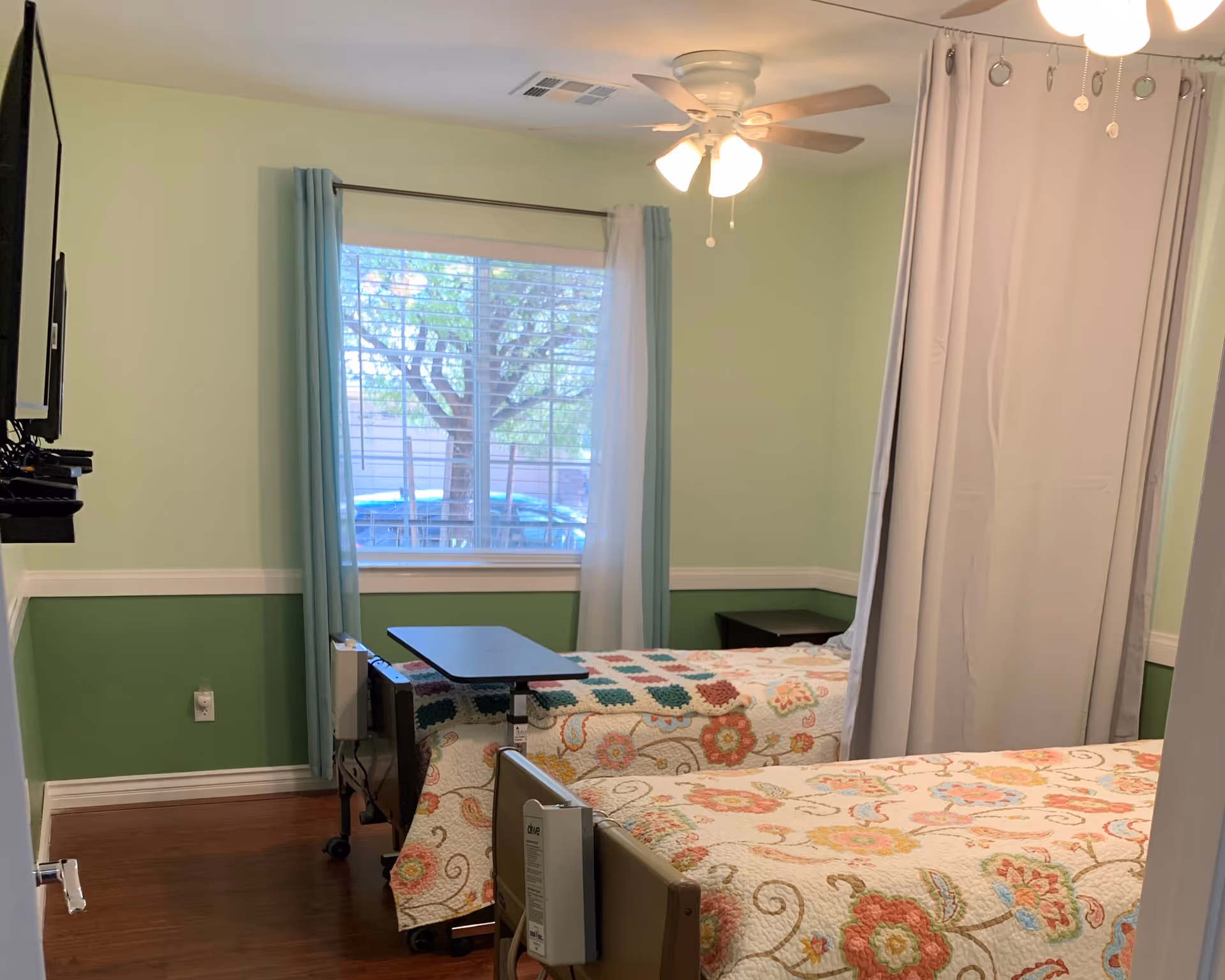 Two twin beds with floral quilts in a pastel green senior living bedroom.