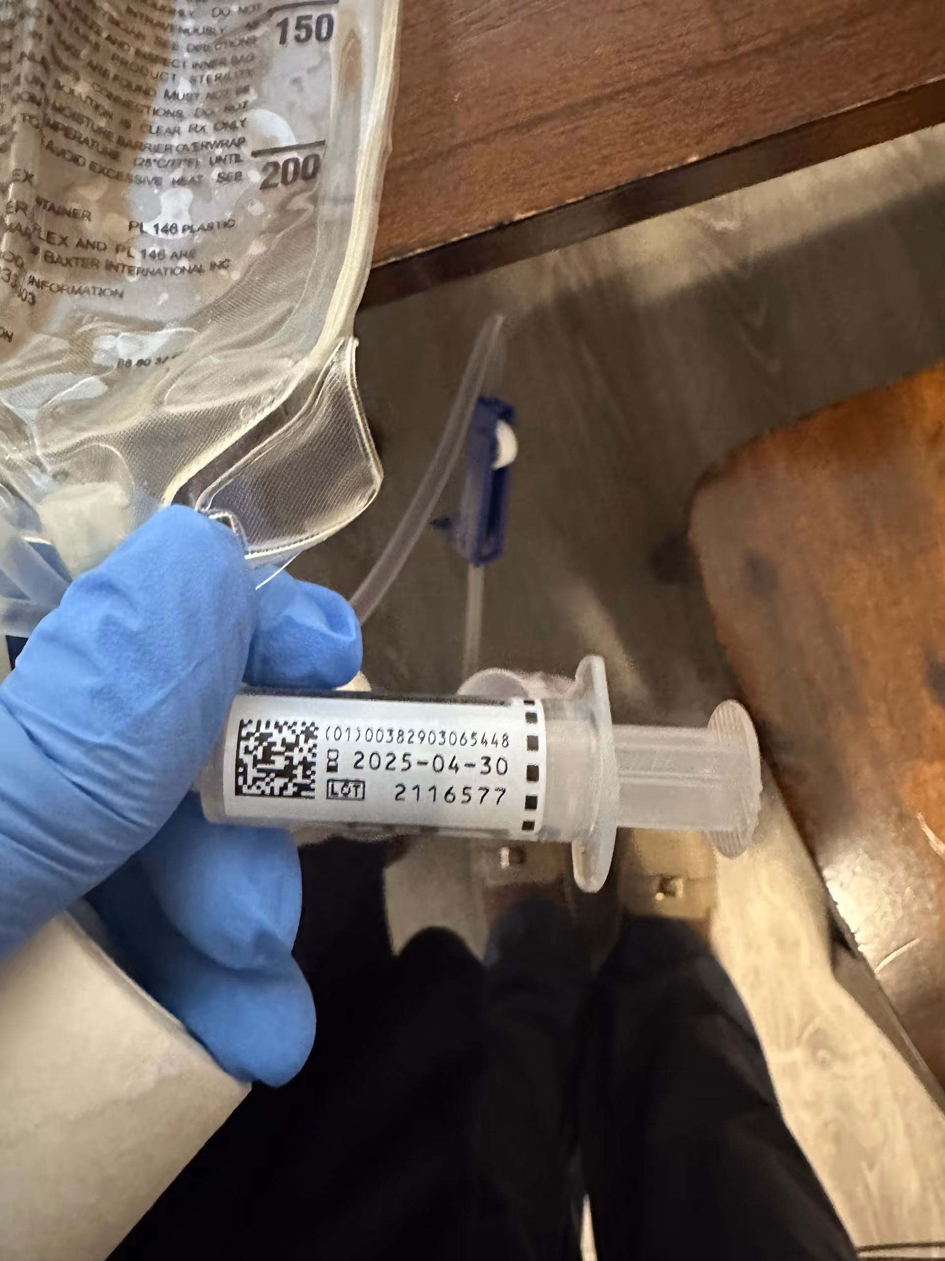 Close up of an IV bag and syringe held by a gloved hand.
