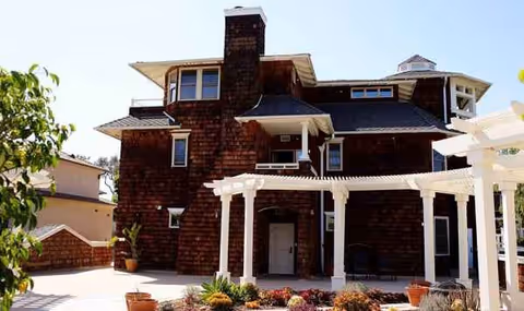 Brick building with a white pergola entrance and potted plants.