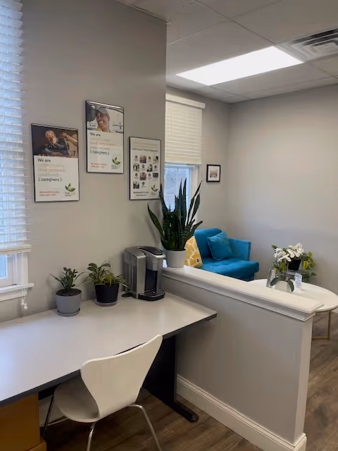 Office-like reception area with a desk, plants, framed posters, and a blue seating corner.