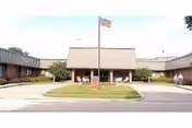 Single-story senior living facility exterior with flagpole, front entrance, and manicured lawn.