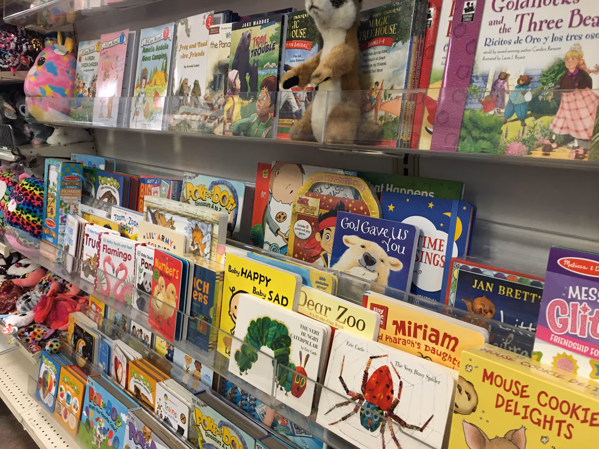 Colorful children's books and plush toys displayed on shelves inside a drugstore.