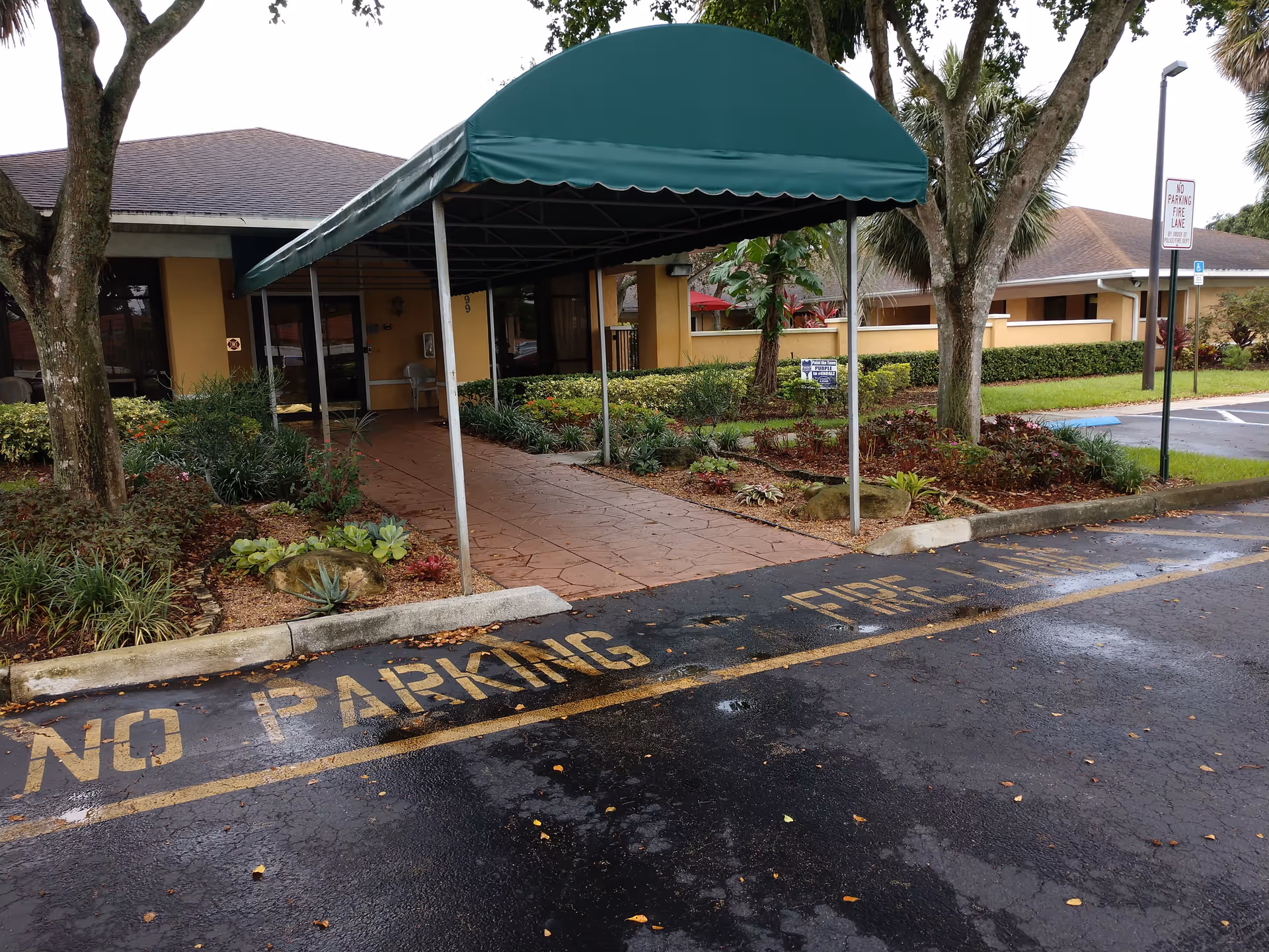Green canopy over walkway leads to the facility entrance with landscaped front yard.