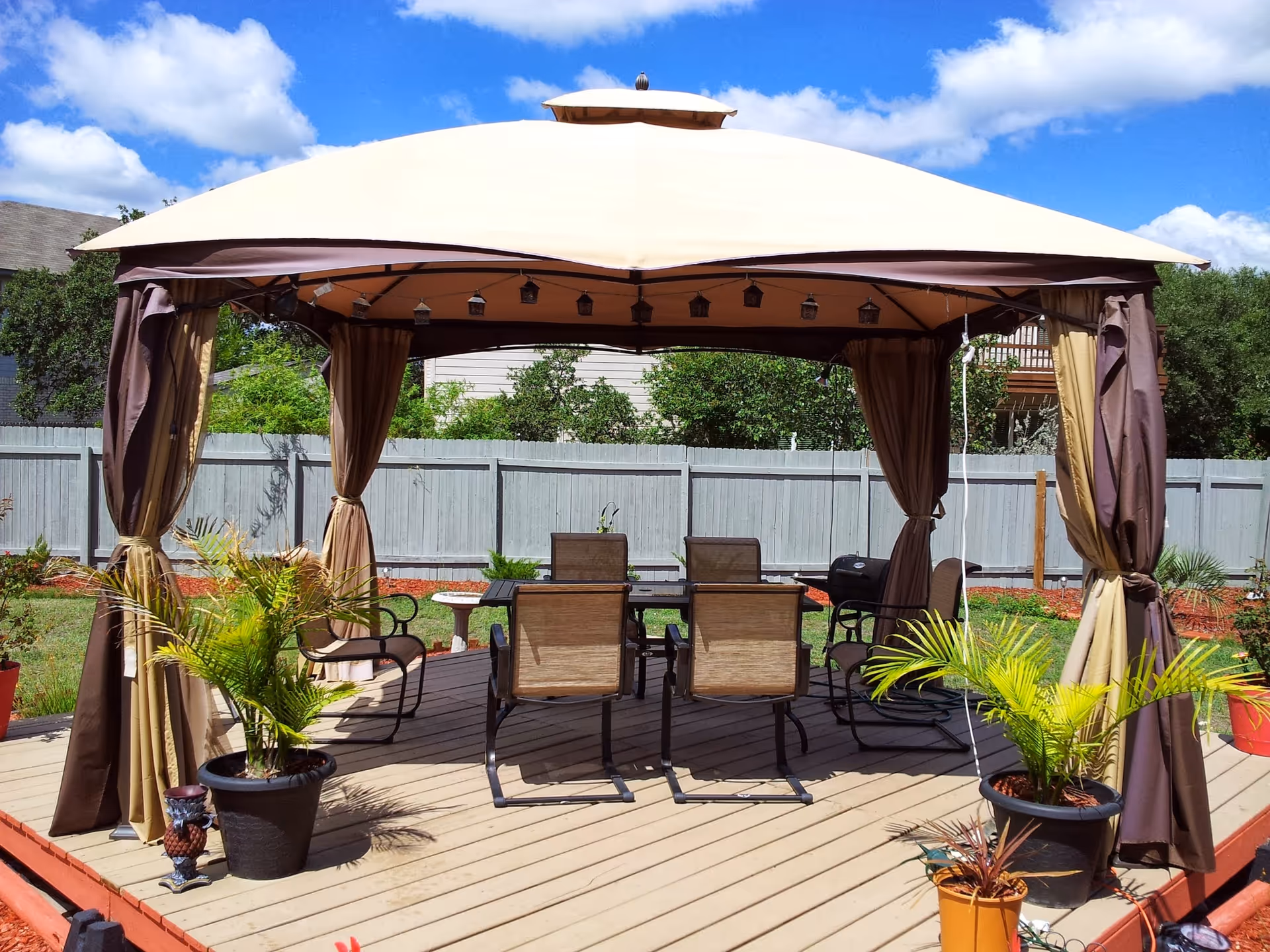 Outdoor gazebo with brown curtains and patio seating on a wooden deck.
